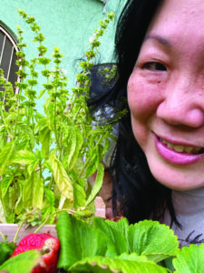 Closeup of margaret cho smiling beside basil and strawberry plants shes grown.